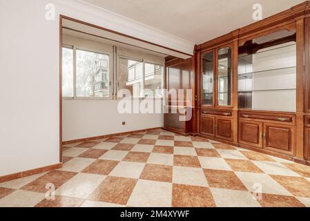 Wooden bookcase with a mirror interior inside the cabinets with glass shelves and stoneware floors in two colors and a wall with two windows facing th Stock Photo