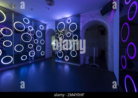 Room of a nightclub decorated with rgb led lights and accesses to other rooms with semicircular arches of white painted bricks Stock Photo