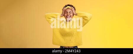 Carefree happy lucky african girl in sweater headband touching head having fun smiling relieved excited laughing out loud close eyes rejoicing spend Stock Photo