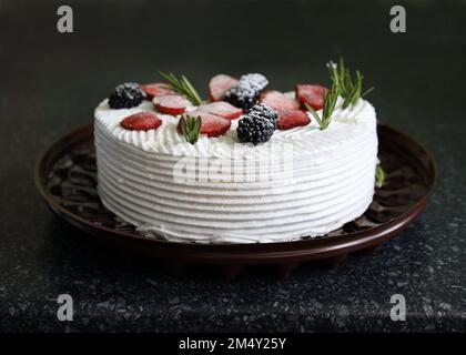 Cake with whipped cream and fruit. Biscuit cake with butter cream close-up. Delicious homemade birthday cake topped with rosemary sprigs, blackberries Stock Photo