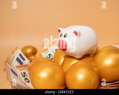 Golden eggs and piggy bank on money. Golden chicken eggs on euro banknotes and coins. Wealth symbol. Savings and investment. Stock Photo