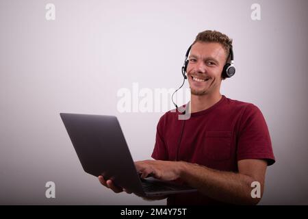 A man is holding a laptop and wearing earphones with a microphone, call center work, studio advertising photo with copy space Stock Photo
