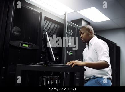 Running diagnostics on your servers. an IT technician using a computer while working in the server room of a data center. Stock Photo