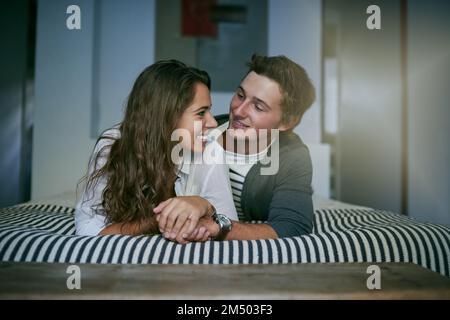 Because he makes me happy. an affectionate young couple lying on bed. Stock Photo