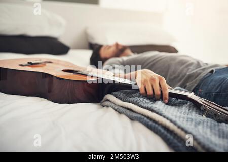 Practising all day has made him very tired. a young handsome man sleeping next to his guitar at home. Stock Photo