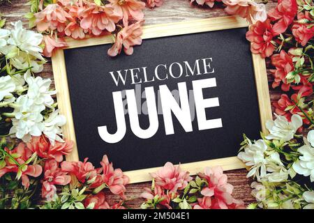 Welcome June typography text written on wooden blackboard with flower bouquet decorate on wooden background Stock Photo