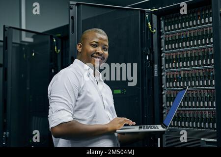 Keeping your computer systems up to date. an IT technician using a laptop while working in a data center. Stock Photo
