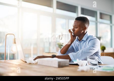 Maybe I should consider going to the doctor tomorrow. a young businessman suffering with a cold while sitting at his desk at work. Stock Photo