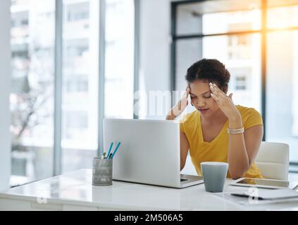I wish this throbbing headache would just go away. a young designer looking stressed out while working in an office. Stock Photo