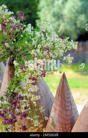 A wreath of wildflowers hangs on pointed wooden pegs of the fence, the holiday of the summer solstice. Stock Photo