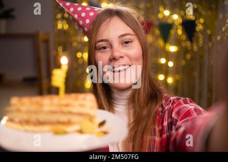 Beautiful blonde woman wearing shirt holding birthday cake and taking selfie photo celebrating at home. Copy space Stock Photo