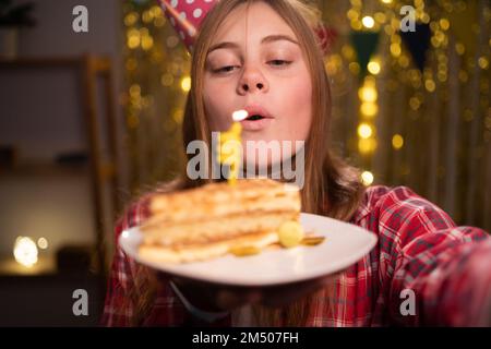 Charming girl blows out the candle on birthday cake. girl with dessert in decor home. She makes a wish. Happy Birthday. Copy space Stock Photo