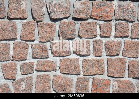 The texture of a wall made of red granite stones. Chopped stones in rows. Stock Photo