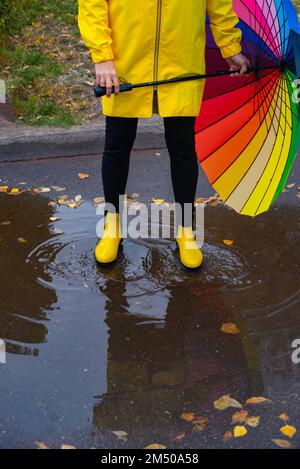 one multi-colored umbrella and yellow boots in a puddle Stock Photo