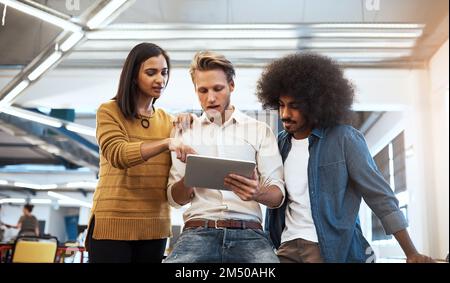 Getting some much needed input. three young businesspeople looking at a tablet in their office. Stock Photo