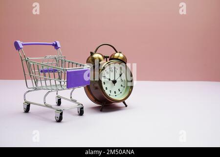 Shopping Mini Trolley cart and alarm clock on pink background Stock Photo