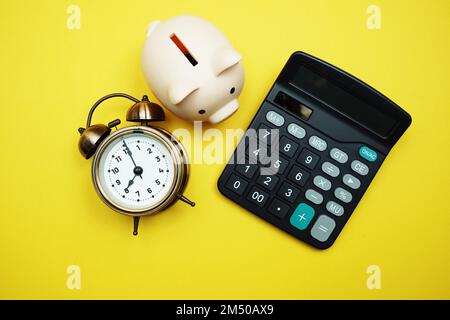 Piggy bank with alarm clock and calculator on yellow background Stock Photo