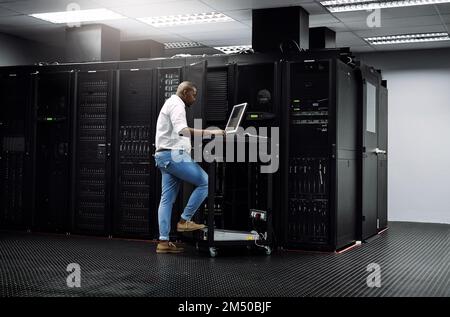 Updating your software. Full length shot of an IT technician using a computer while working in the server room of a data center. Stock Photo