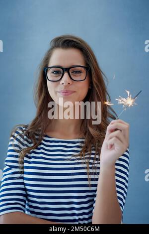 Dont be afraid to sparkle. Studio shot of a beautiful young woman holding sparklers against a blue background. Stock Photo