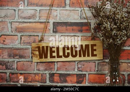 Welcome sign text message on wooden board hanging on old brick wall background Stock Photo