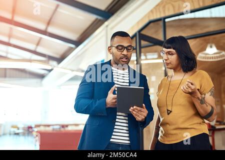 Heres what the client wants...two designers working on a digital tablet together in an office. Stock Photo