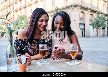 Two women drinking beer and using a mobile outdoors Stock Photo