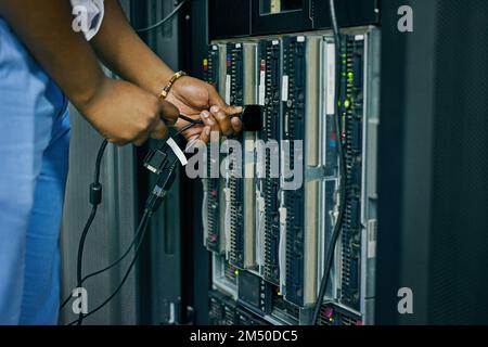 Plugged in to professional IT administration. an IT technician plugging cables into a computer in a data center. Stock Photo