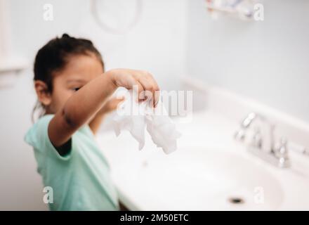 A cute preschool girl practicing good hygiene using the bathroom sink as she washes up Stock Photo