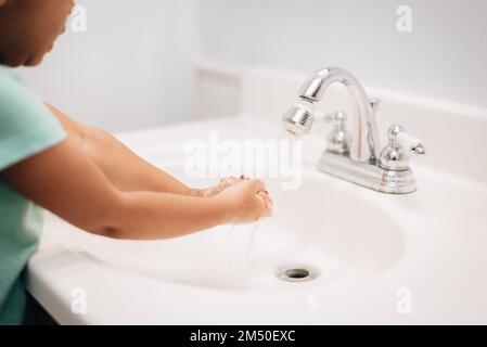 A cute preschool girl practicing good hygiene using the bathroom sink as she washes up Stock Photo