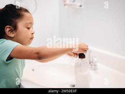 A cute preschool girl practicing good hygiene using the bathroom sink as she washes up Stock Photo