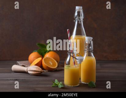 fresh orange juice in three bottles with citrus fruits on  a brown wooden background. Rustic concept. Front view image Stock Photo
