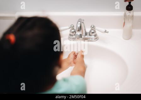 A cute preschool girl practicing good hygiene using the bathroom sink as she washes up Stock Photo