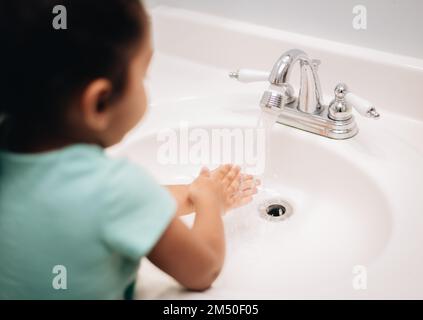 A cute preschool girl practicing good hygiene using the bathroom sink as she washes up Stock Photo