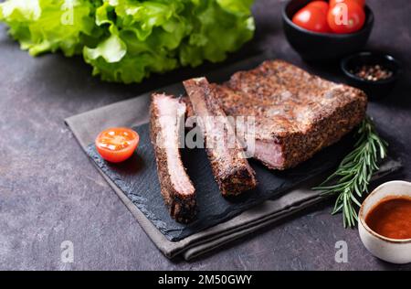 Juicy barbecue pork ribs with tomatoes, sauce and fresh salad on a dark background.  Picnic product concept. Copy space. Stock Photo