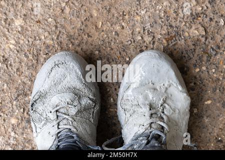 Sneakers heavily stained in grey paint on an asphalt Stock Photo