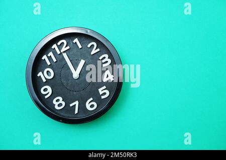 Black round clock showing Ten o'clock on green background Stock Photo