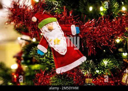 Handmade coloured thin felt Santa Claus hanged in a Christmas Tree with shining lights Stock Photo