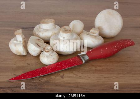 White champignons and a red knife on the table. Ingredients for cooking. Stock Photo