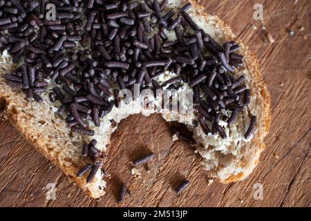 Wholemeal bread spread with butter and delicious chocolate sprinkles on top, on wooden board. A bite has been taken Stock Photo
