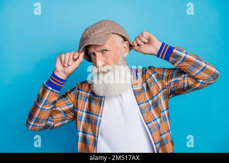 Photo of serious attractive retired man dressed plaid suit put on headwear isolated blue color background Stock Photo
