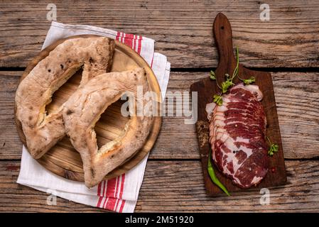 Serbian traditional homemade baked buns( lepinja) and cutting board with sliced prosciutto on wooden table. Stock Photo
