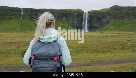 Woman with backpack looking at Seljalandsfoss waterfall Iceland Stock Photo