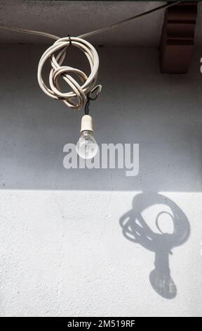 Old light bulb hanging from a ledge with the excess cord coiled up. Perfect shadow on wall Stock Photo