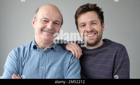 Happy mature senior father and grown son standing together, hugging, looking at camera Stock Photo
