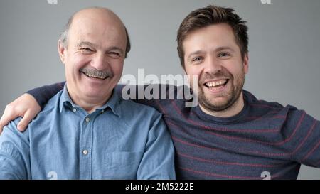 Happy mature senior father and grown son standing together, hugging, looking at camera Stock Photo