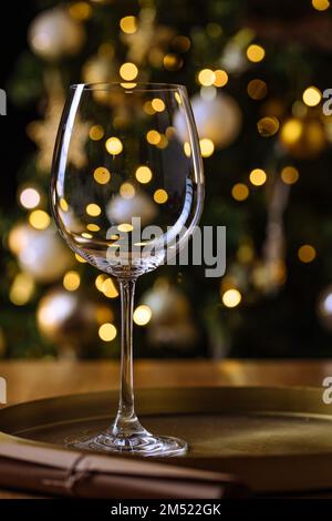 Empty elegant wine glass in front of Christmas tree with new year party lights in background Stock Photo