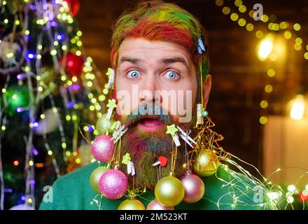 Surprised bearded man with decorated beard for holidays. Merry Christmas and Happy new year. Stock Photo