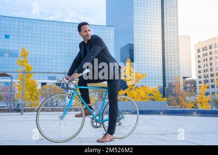 Young stylish businessman going to work by bicycle in front of financial district. Stock Photo