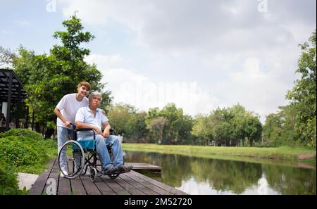 Asian careful caregiver or nurse hold the patient hand and encourage the patient in a wheelchair. Concept of happy retirement with care from a caregiv Stock Photo