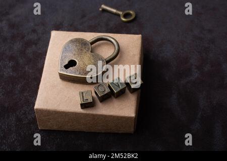 Love shaped padlock, key and love wording placed on box Stock Photo